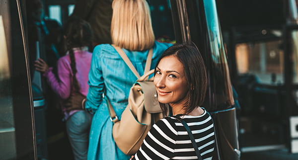 A line of passengers enter a charter bus, with one woman turning back to smile